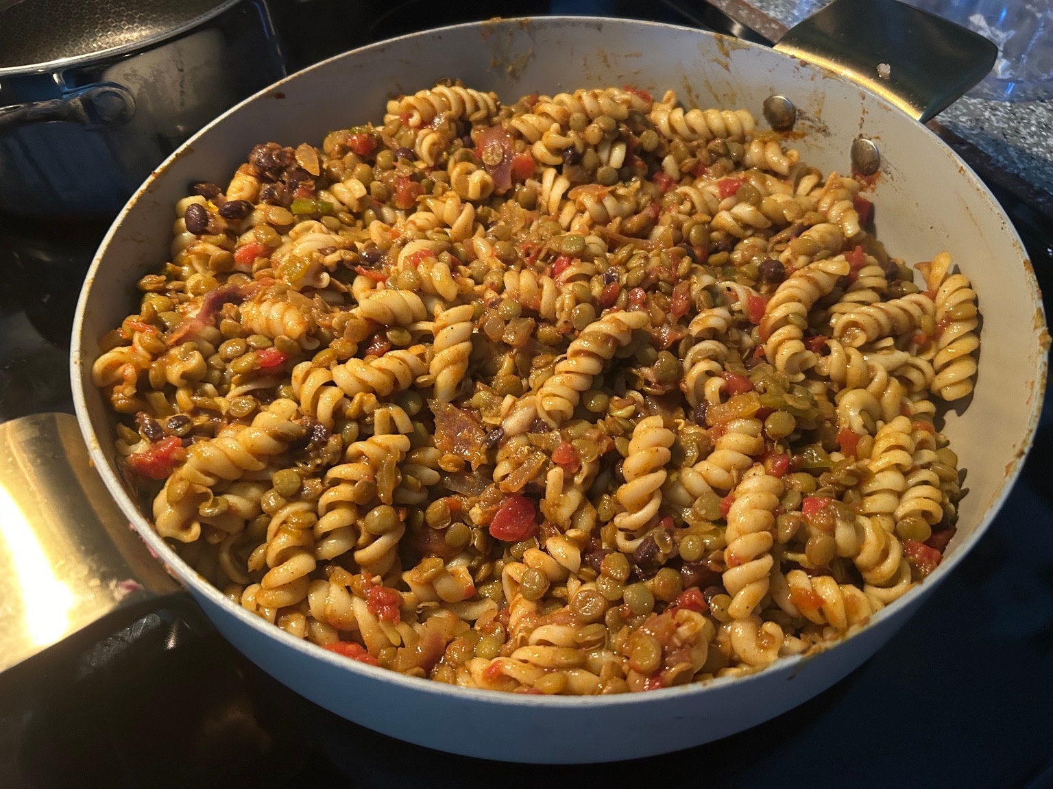 Finished rotini with lentils, black beans and tomatoes in a skillet.