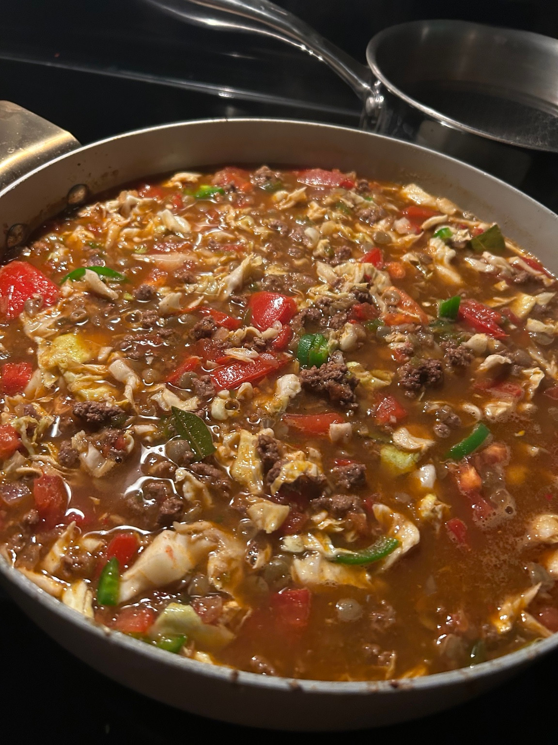 Close view of the Founder’s tomato-broth stew with crumbled beef, cabbage and green jalapeño pieces in a skillet.